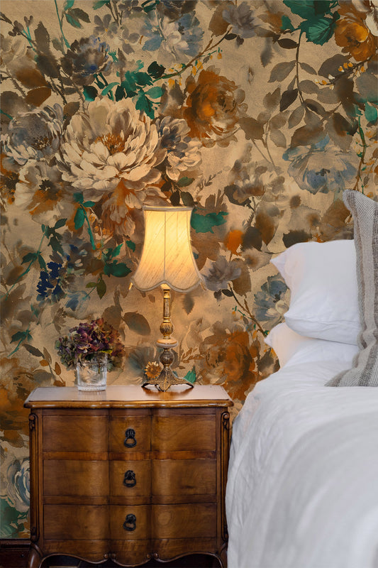 A styled bedroom corner featuring a large floral wallpaper mural with cream, gold, and green botanical patterns, a wooden nightstand, a lit table lamp, and a white bed.