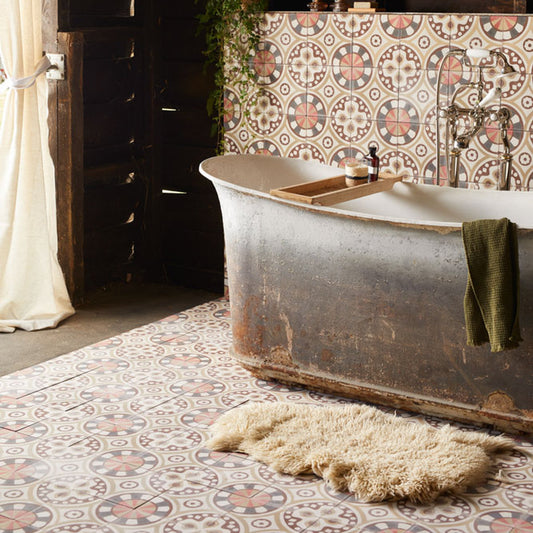 A rustic vintage-style bathtub in a bathroom setting with patterned ceramic tiles, a cream shag rug, and a dark green towel draped over the side.