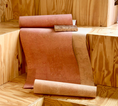 A roll of textured cork or cork-like flooring material partially unrolled on wooden steps, with a second roll placed in front and a small rectangular sample piece resting on top.