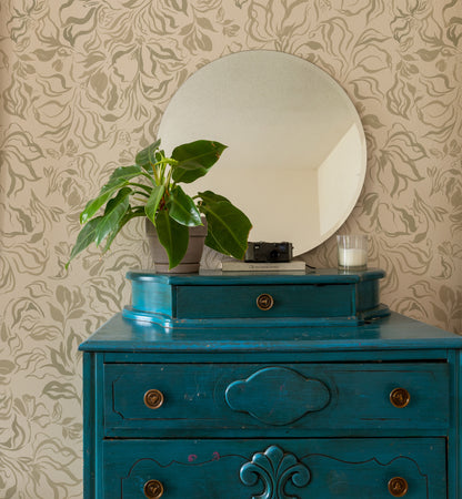 A distressed teal blue wooden dresser with brass knobs, topped with a potted green plant, a round mirror, and small decorative items, set against a beige patterned wallpaper background.