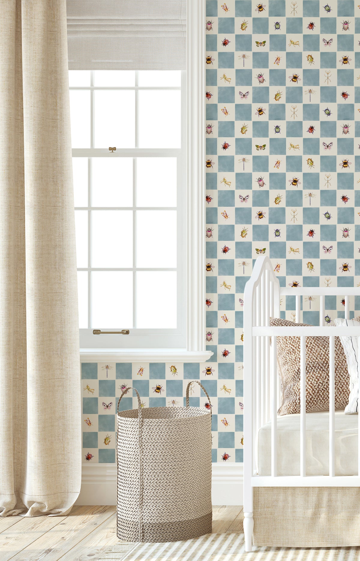 A styled nursery corner featuring light blue checkered wallpaper with small multicolored insect illustrations, a white wooden crib, a beige curtain, and a woven basket on a light wood floor.