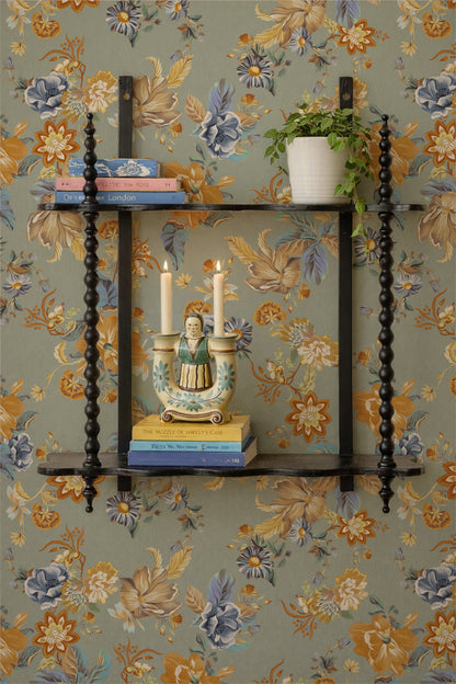 A decorative black wooden wall shelf with three tiers and turned spindles, styled with books, a ceramic candle holder, and a potted plant against a floral wallpaper background.