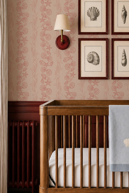 A styled nursery corner featuring a wooden crib with a white mattress and a light blue blanket, set against pink starfish-patterned wallpaper and a dark wood headboard. A red wall sconce and framed seashell artwork are visible on the wall.