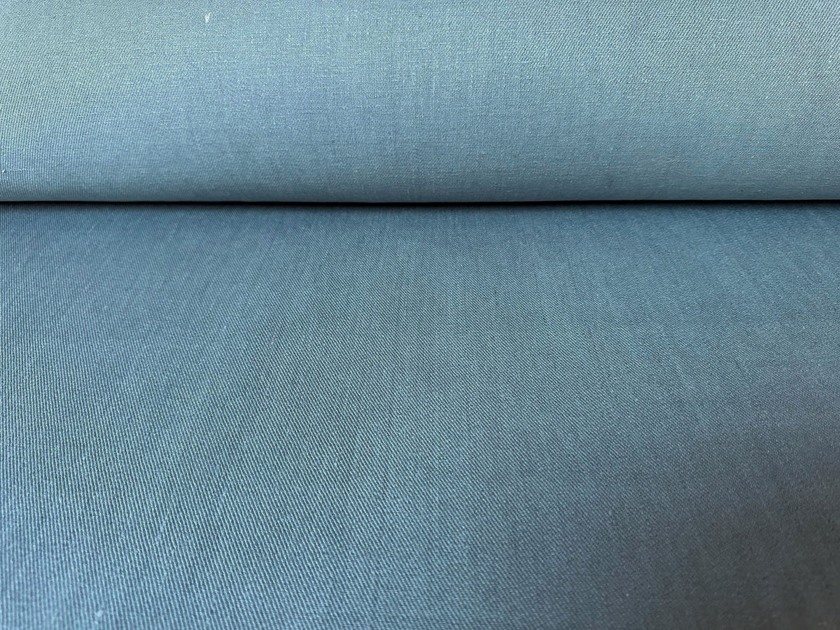 A close-up of a textured fabric, likely upholstery fabric, in a muted slate blue or dusty teal color, shown with a folded top edge.
