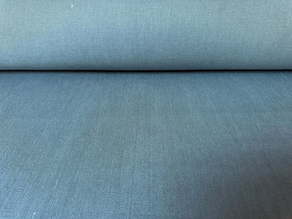 A close-up of a textured fabric, likely upholstery fabric, in a muted slate blue or dusty teal color, shown with a folded top edge.