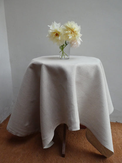 White tablecloth on a small round table with a vase of white flowers against a plain wall.