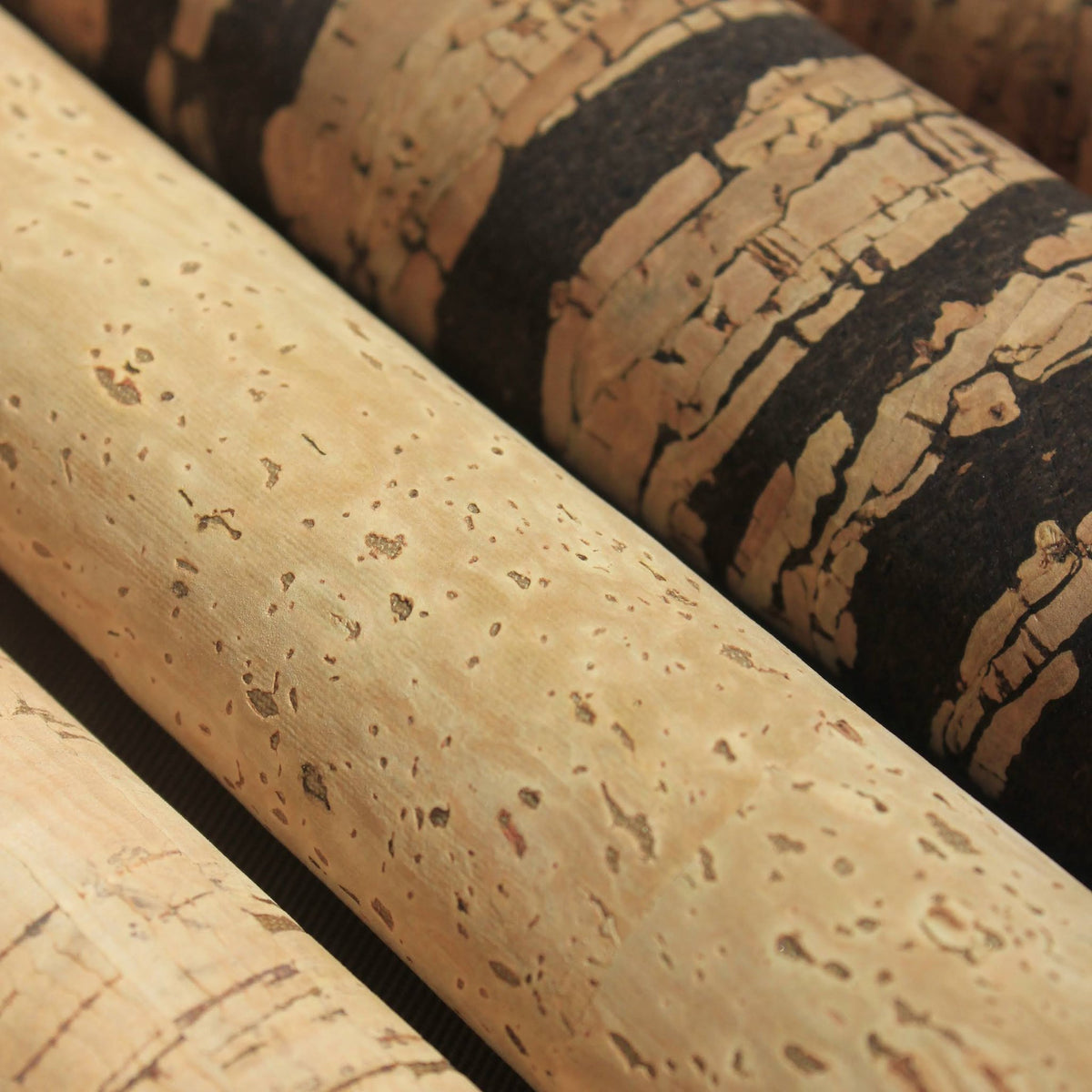 Close-up of rolled cork material in two tones: a light tan cork with small darker speckles and a darker brown-black cork with lighter streaks.