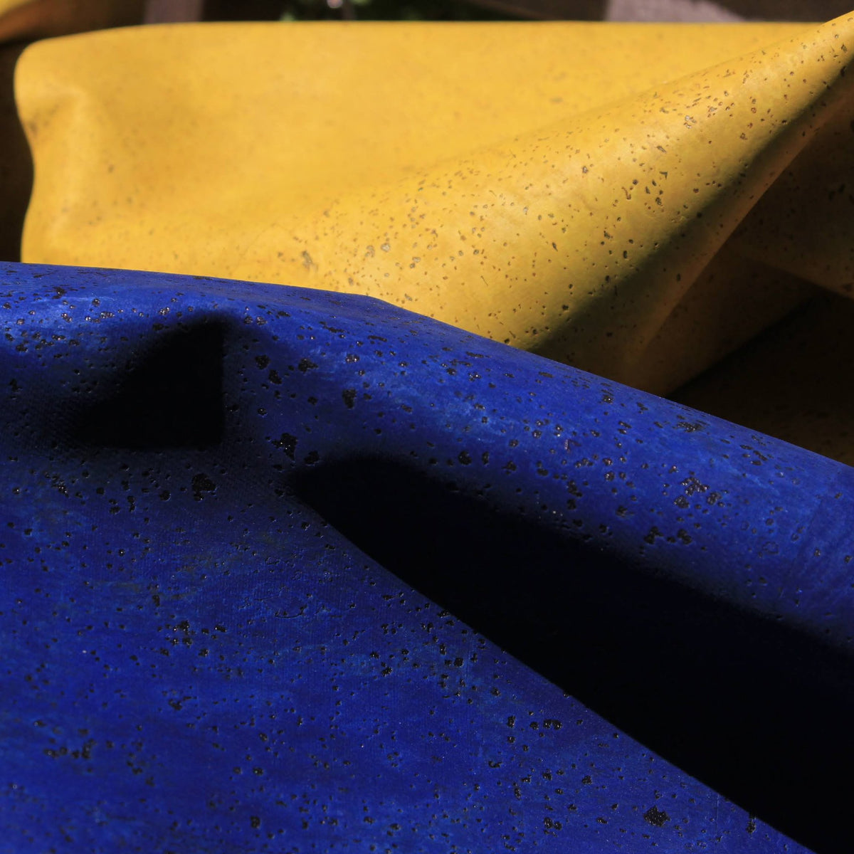 A close-up of draped fabric in two colors: a bright royal blue in the foreground with dark speckles, and a mustard yellow fabric in the background with lighter golden speckles.
