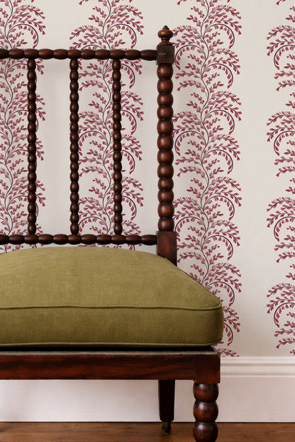 A close-up of a dark wood spindle-back chair with an olive green cushion, set against a wall with cream wallpaper featuring a burgundy floral vine pattern.