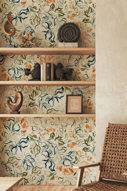 A styled interior corner showing a wall covered in a vintage-style botanical wallpaper with swirling blue, green, and orange floral motifs on a warm cream background. Built-in wooden shelves display decorative objects, and part of a woven rattan chair is visible in the foreground.