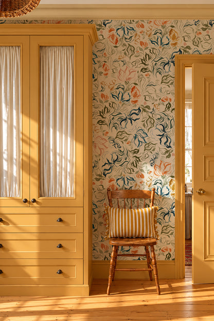 A styled interior room corner featuring floral wallpaper with blue, orange, and green botanical motifs on a cream background, next to a mustard yellow wooden wardrobe and a small wooden chair with a striped cushion.