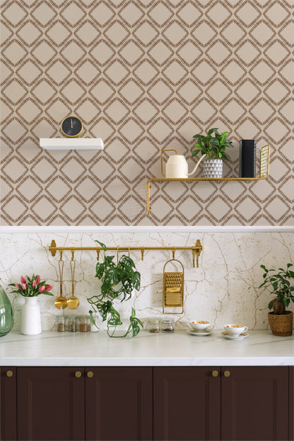 A styled kitchen interior featuring beige wallpaper with a brown geometric trellis pattern on the upper wall, a white marble countertop, dark brown cabinets, gold wall hardware, and several potted green plants.