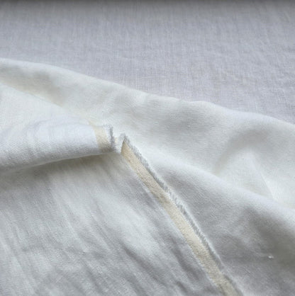 A close-up of off-white fabric with a visible fold and raw, slightly frayed edge, showing a light tan underside.