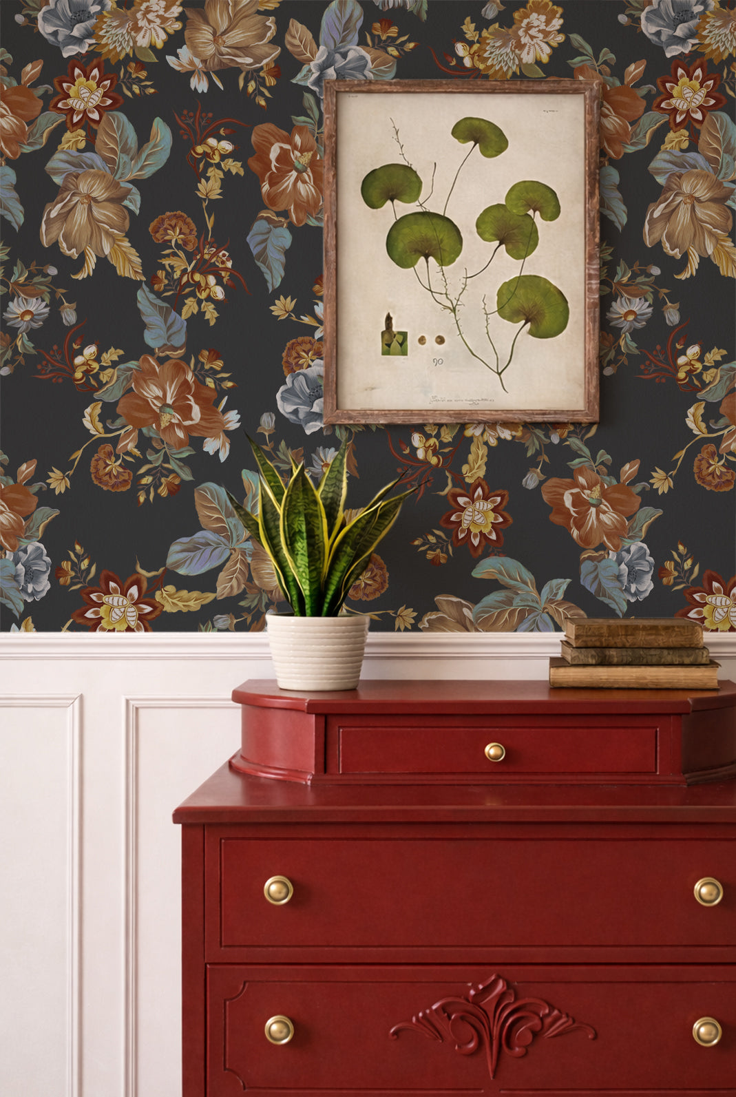 A styled interior scene showing floral wallpaper in dark charcoal with muted orange, beige, and blue botanical motifs, a framed botanical print on the wall, a red wooden dresser, and a potted snake plant.