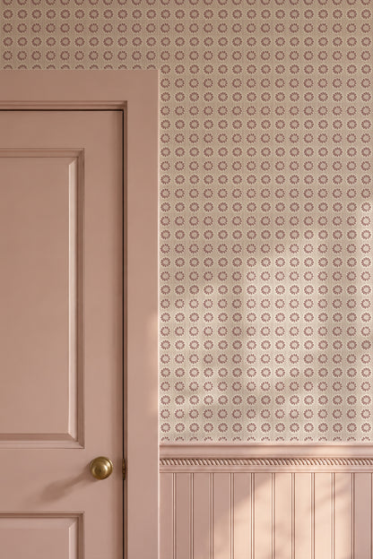 A close-up of a dusty pink interior wall with a repeating circular geometric pattern on the upper section and wainscoting below, alongside a matching pink paneled door with a brass doorknob.