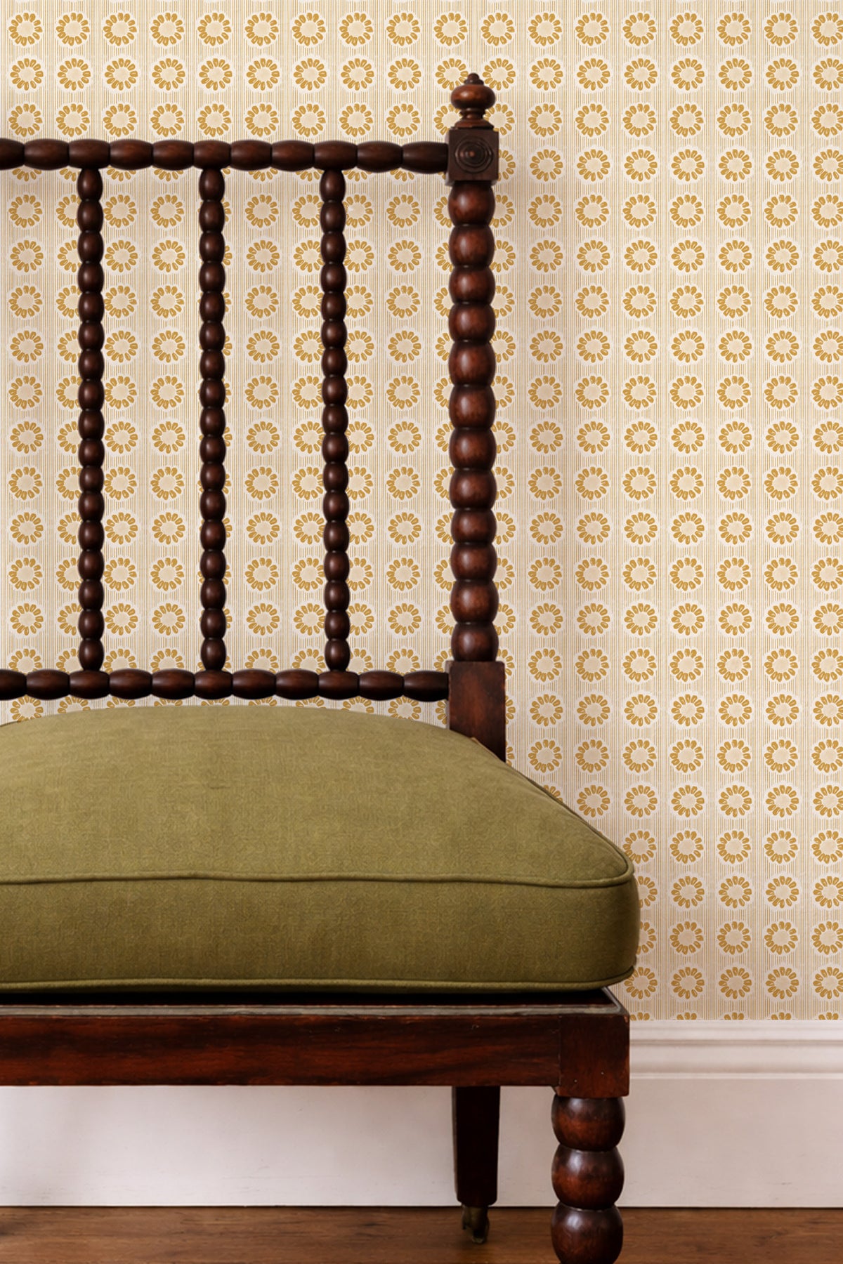 A close-up of a dark wood spindle-back chair with an olive green upholstered seat cushion, set against a patterned wallpaper background.