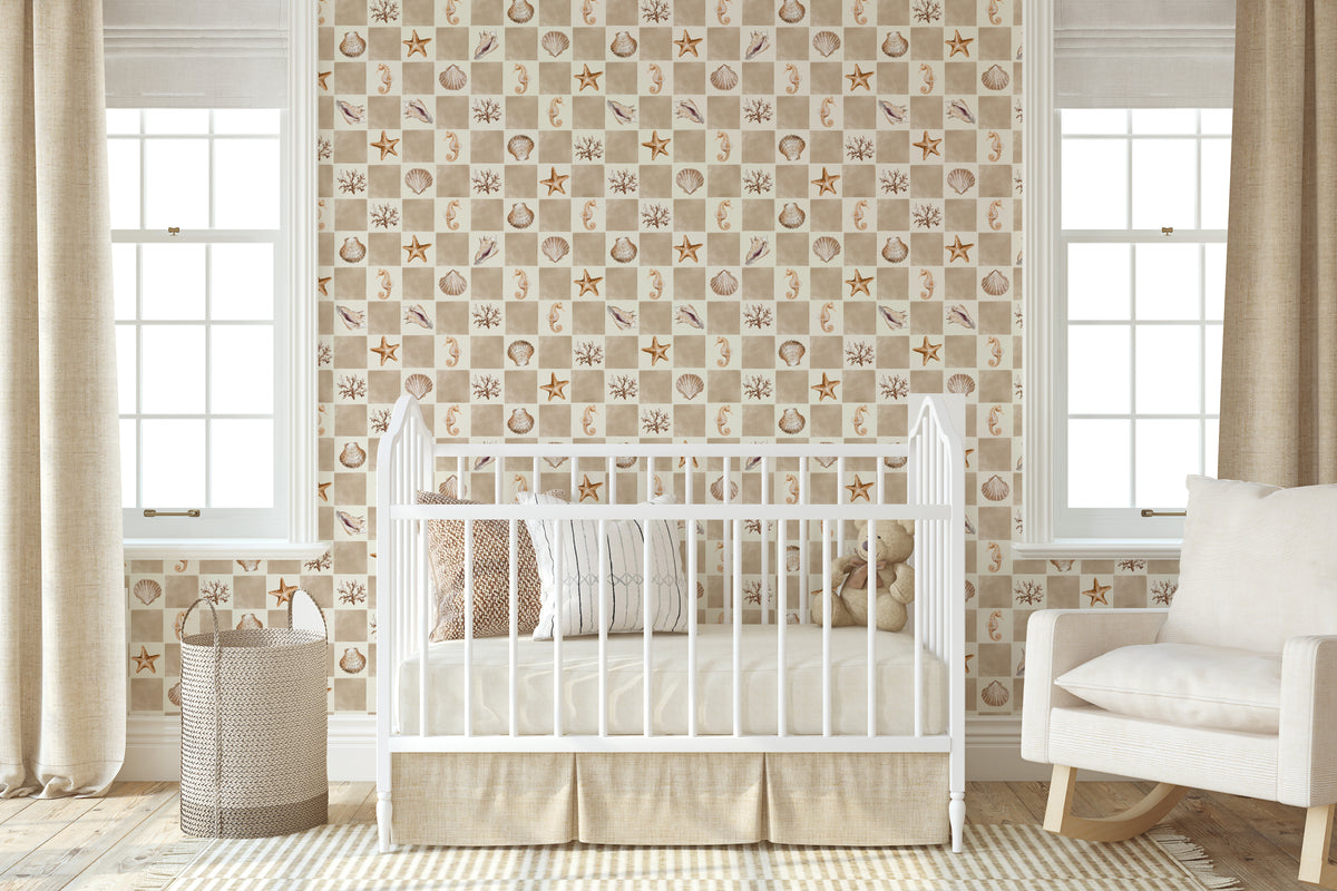 A styled nursery room featuring a white wooden crib with a ruffled skirt, set against a wall with nautical-themed wallpaper. The wallpaper has a beige and white checkered pattern with illustrations of seashells, starfish, and small boats.