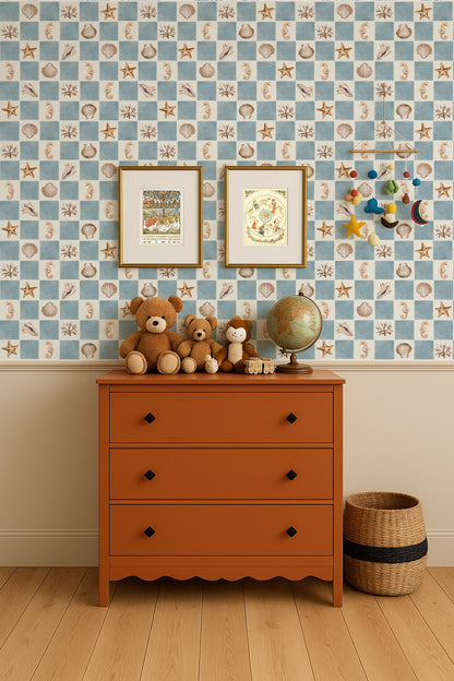 A styled children's room corner featuring a terracotta orange three-drawer dresser against a blue and beige seashell-patterned wallpaper. Decorative items on the dresser include two brown teddy bears, a vintage-style globe, and small wooden figurines.