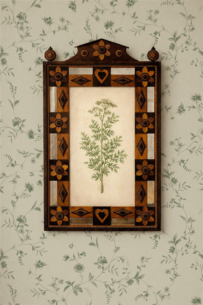 A framed botanical art print featuring a green herb illustration on an off-white background, surrounded by an ornate geometric border in dark brown, tan, and cream. The framed piece is mounted on a light green floral wallpaper.