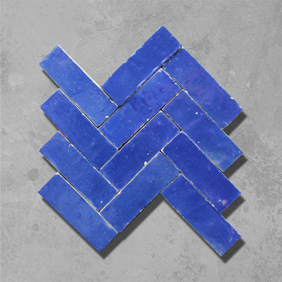 Blue ceramic subway mosaic tiles arranged in a herringbone pattern on a textured gray concrete background.