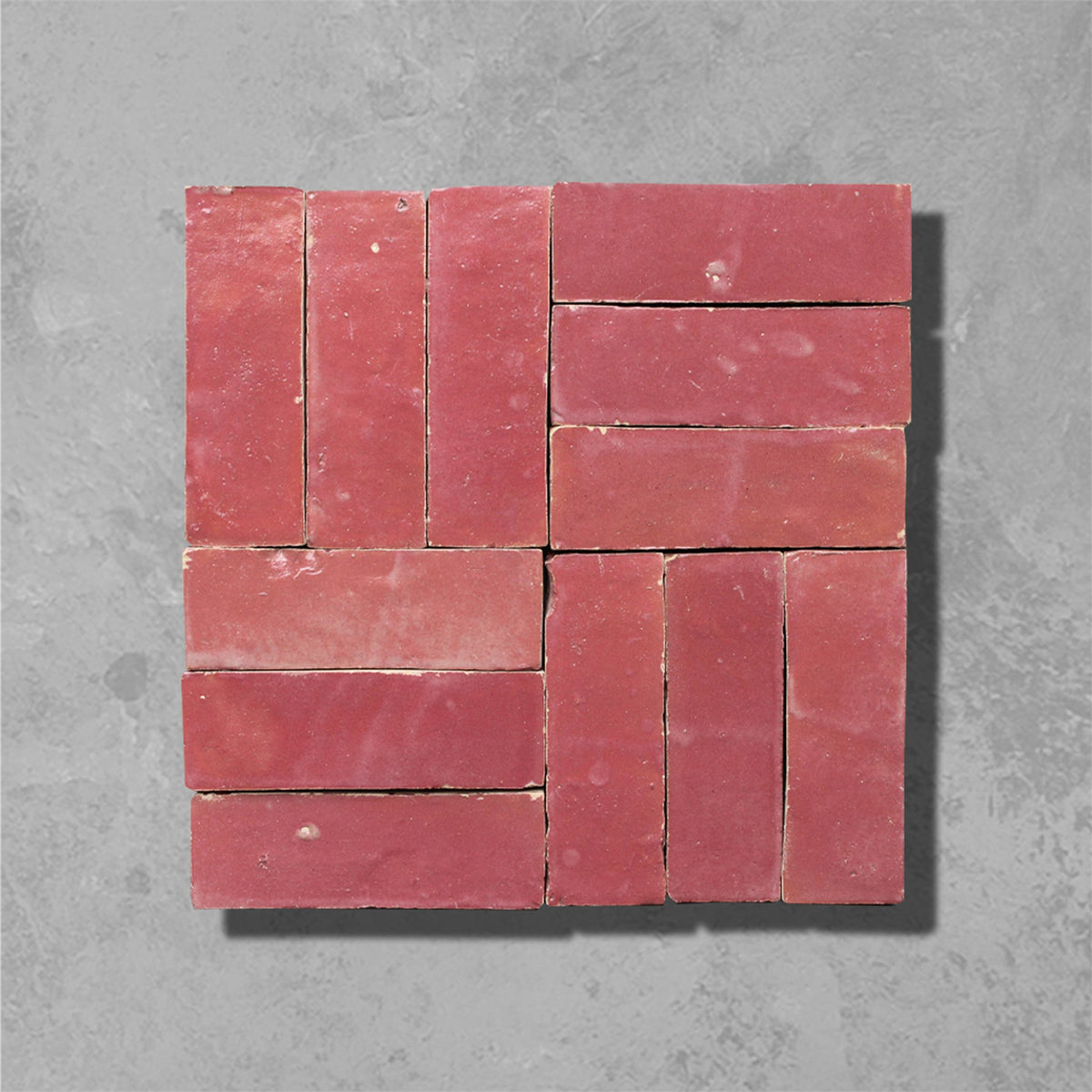 A square arrangement of terracotta red clay bricks with a rustic finish, arranged in a grid pattern against a textured gray concrete background.