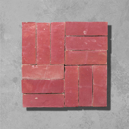 A square arrangement of terracotta red clay bricks with a rustic finish, arranged in a grid pattern against a textured gray concrete background.